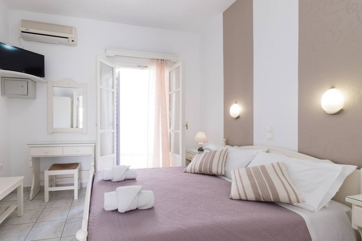A bedroom with a bed, bedside tables, a desk, a chair, an air conditioner, and a window with curtains.