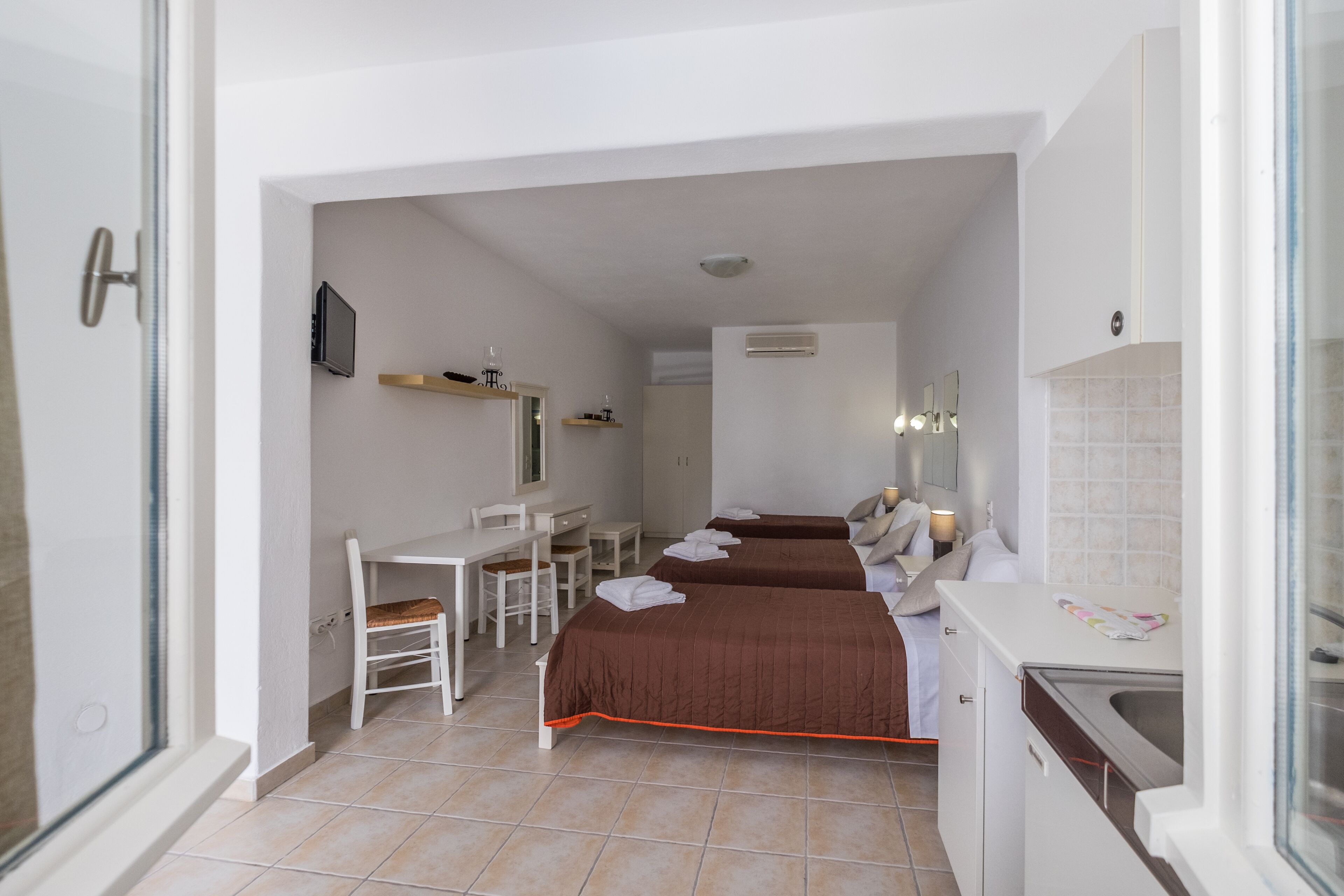 Une chambre d’hôtel avec deux lits, un bureau, une chaise, une télévision et une kitchenette.