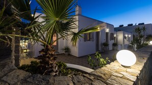 Un edificio blanco con un camino de piedra, una palmera y una luz esférica iluminada.