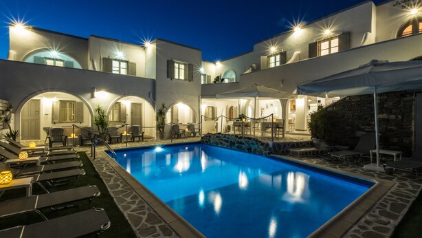 Zona junto a la piscina con sillones de descanso y una pileta, rodeada por un edificio con arcos y mesas al aire libre.
