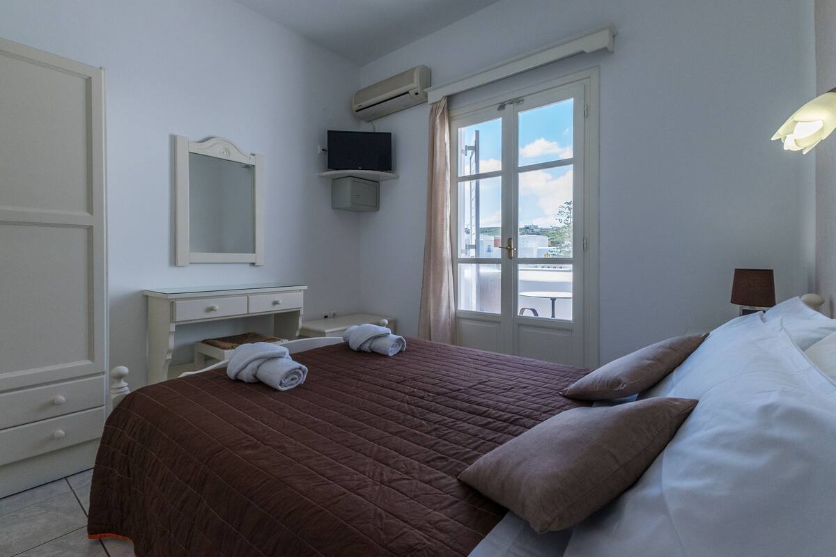 A hotel room with a bed, a TV, a window with curtains, a desk, and a chair.