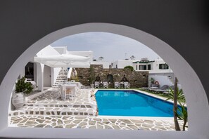 A pool area with stone flooring, white furniture, and a stone wall in the background. - Joseph Studios (Paros)