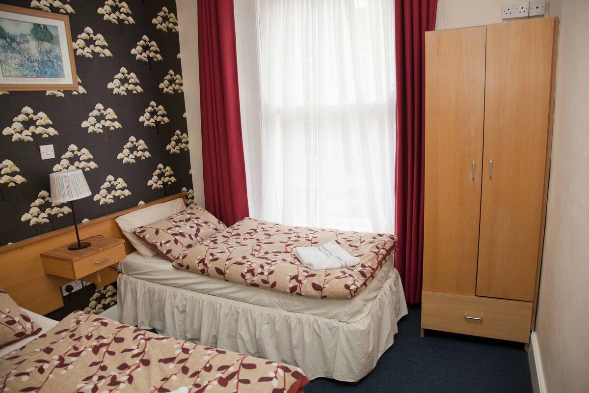 Un dormitorio con cama, mesita de noche, armario y ventana con cortinas.