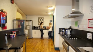 A kitchen with wooden floors, a fire extinguisher, a microwave, and a sink. - Ashfield Hostel (Dublin)