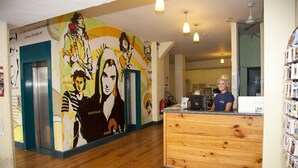 A reception area with a wooden counter, a mural with various figures, and a ceiling fan. - Ashfield Hostel (Dublin)