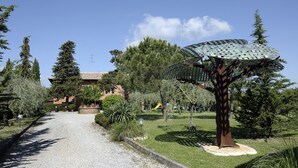 A pathway leading to a building with a tiled roof, surrounded by trees and a metal sculpture. - Hotel Villa Belvedere (San Gimignano)