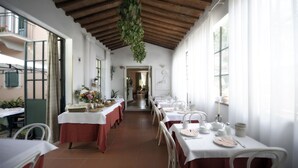 A long dining hall with tables set for a meal, a wooden ceiling, and a view of the outside. - Hotel Villa Belvedere (San Gimignano)
