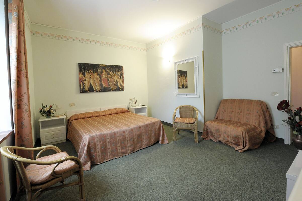 Een slaapkamer met twee eenpersoonsbedden, een stoel, een bank, een schilderij en een spiegel.