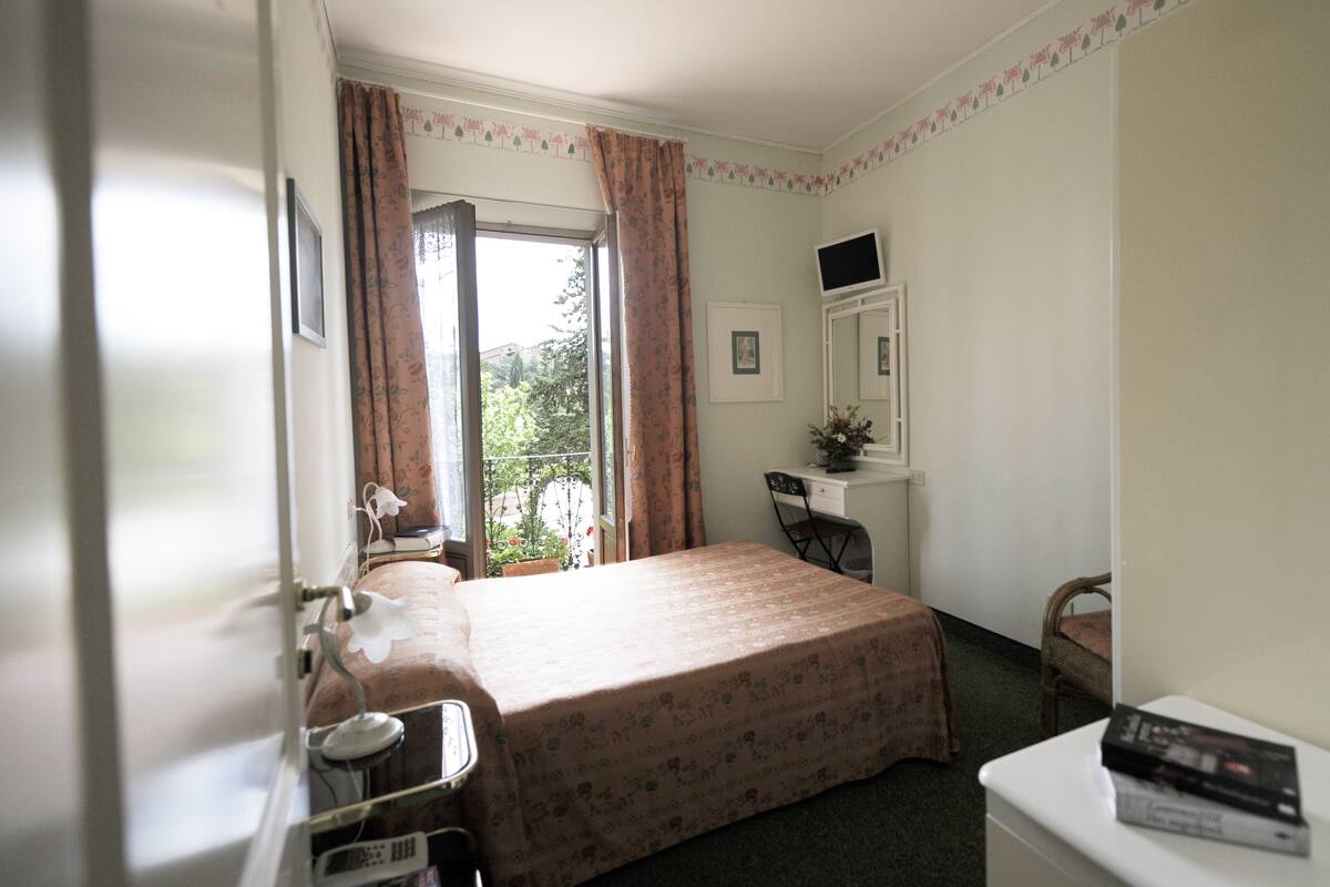Een hotelkamer met een bed, een bureau, een stoel, een televisie en een raam met gordijnen.