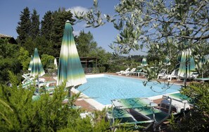 A pool area with lounge chairs and umbrellas, surrounded by greenery and trees. - Hotel Villa Belvedere (San Gimignano)