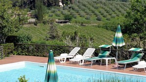A pool area with lounge chairs and umbrellas, surrounded by greenery and hills in the background. - Hotel Villa Belvedere (San Gimignano)