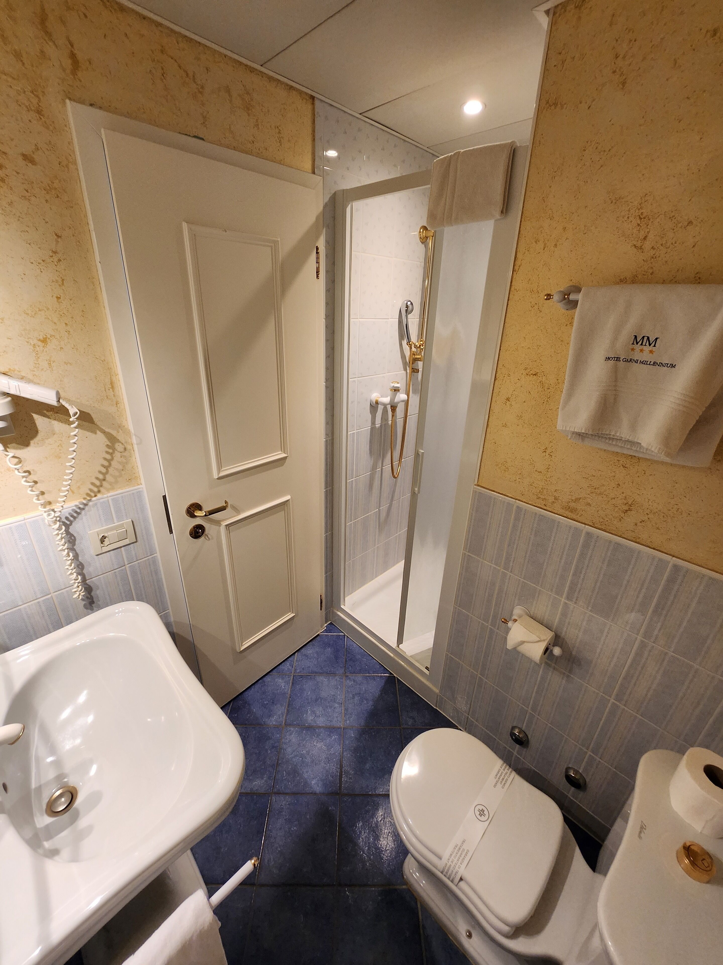 Un baño con ducha, inodoro, lavamanos y toalla colgada en la pared.