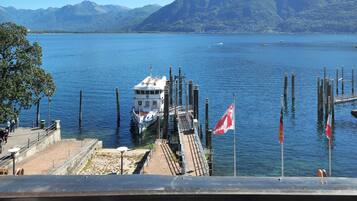 A waterfront dock with a boat, flags, and mountains in the background.