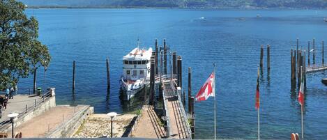 A waterfront dock with a boat, flags, and mountains in the background.