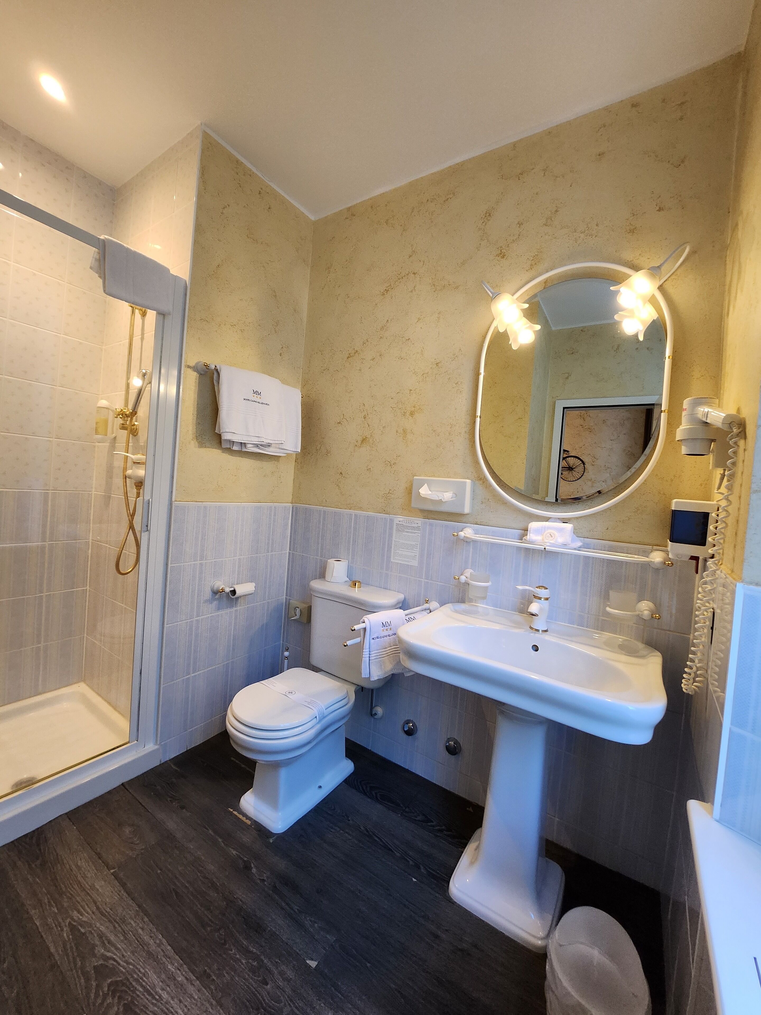 A bathroom with a walk-in shower, toilet, sink, and a mirror with lights.
