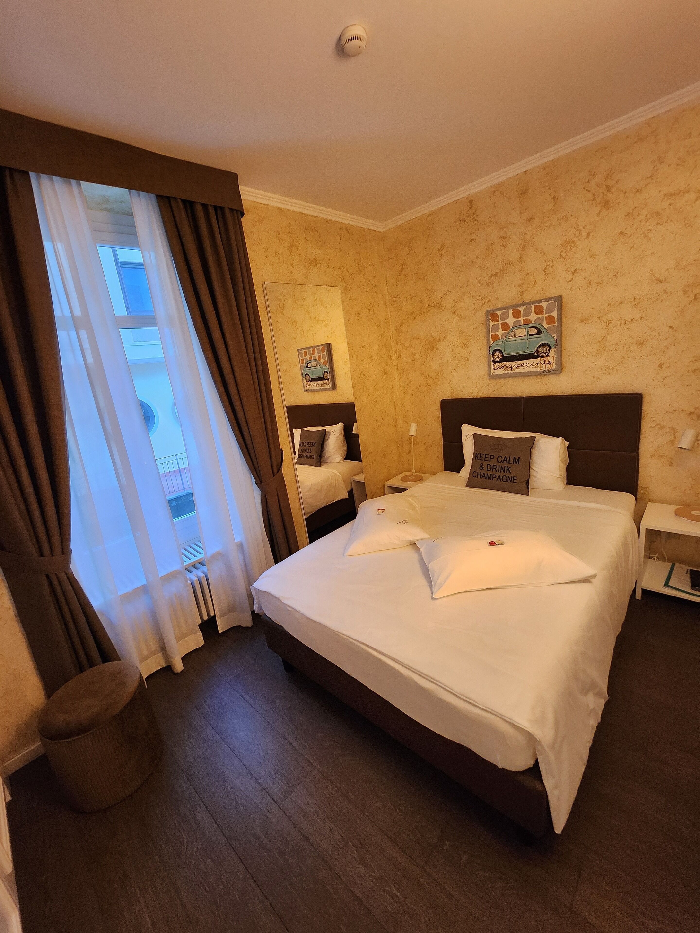 Ein Hotelzimmer mit einem großen Bett, einem Nachttisch, Vorhängen vor dem Fenster und einer Wand mit einer Automobil-Dekoration.