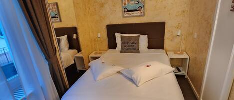 A hotel room with a large bed, two bedside tables, a nightstand, a wall clock, and a window with curtains.