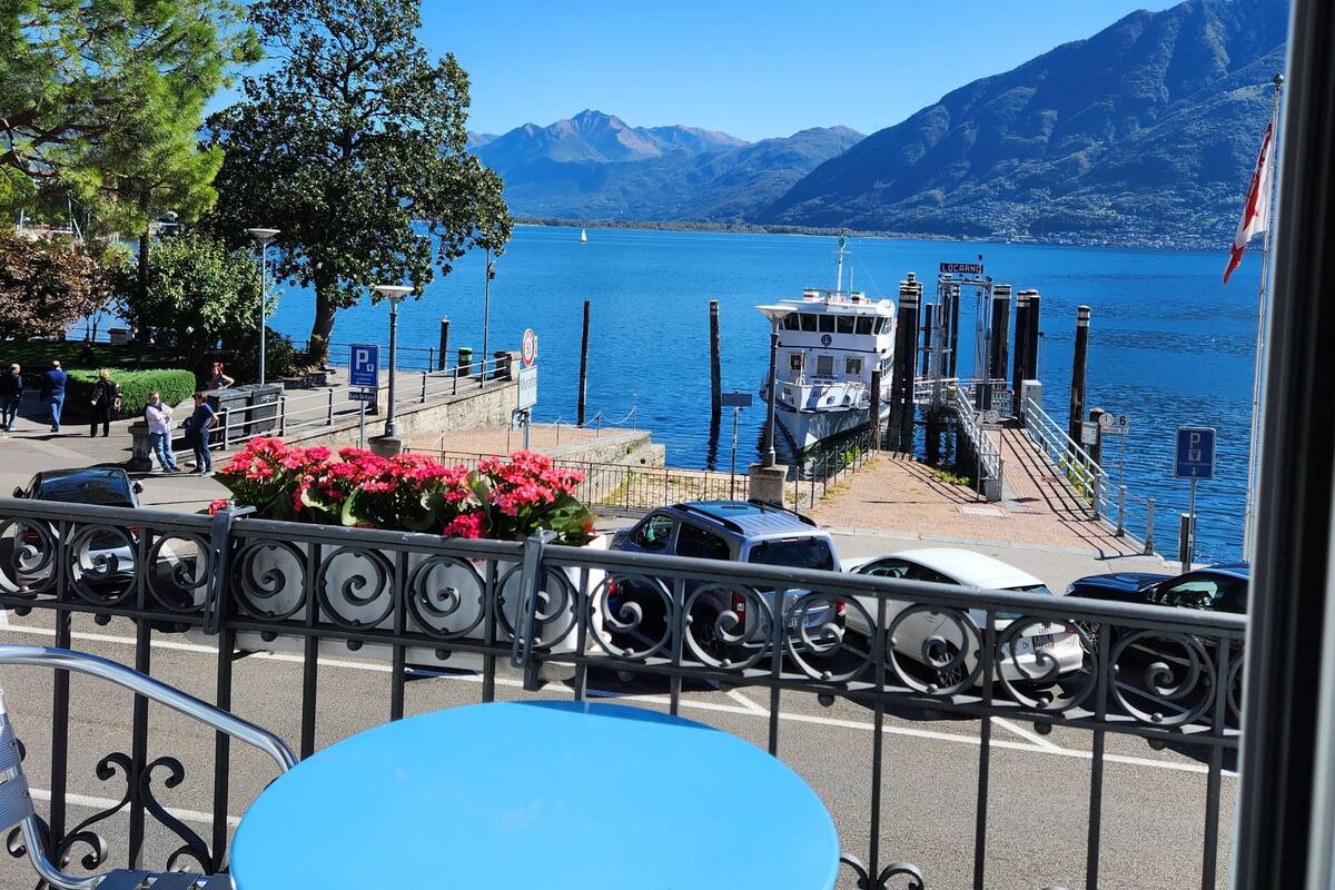 A balcony with a view of a lake, a boat dock, and mountains in the background.
