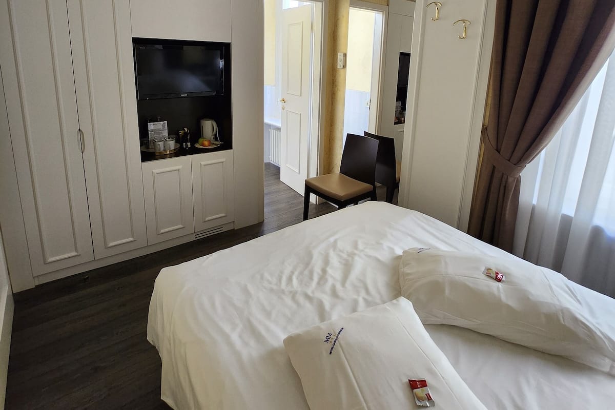 A hotel room with a bed, a TV, a chair, and a wardrobe.