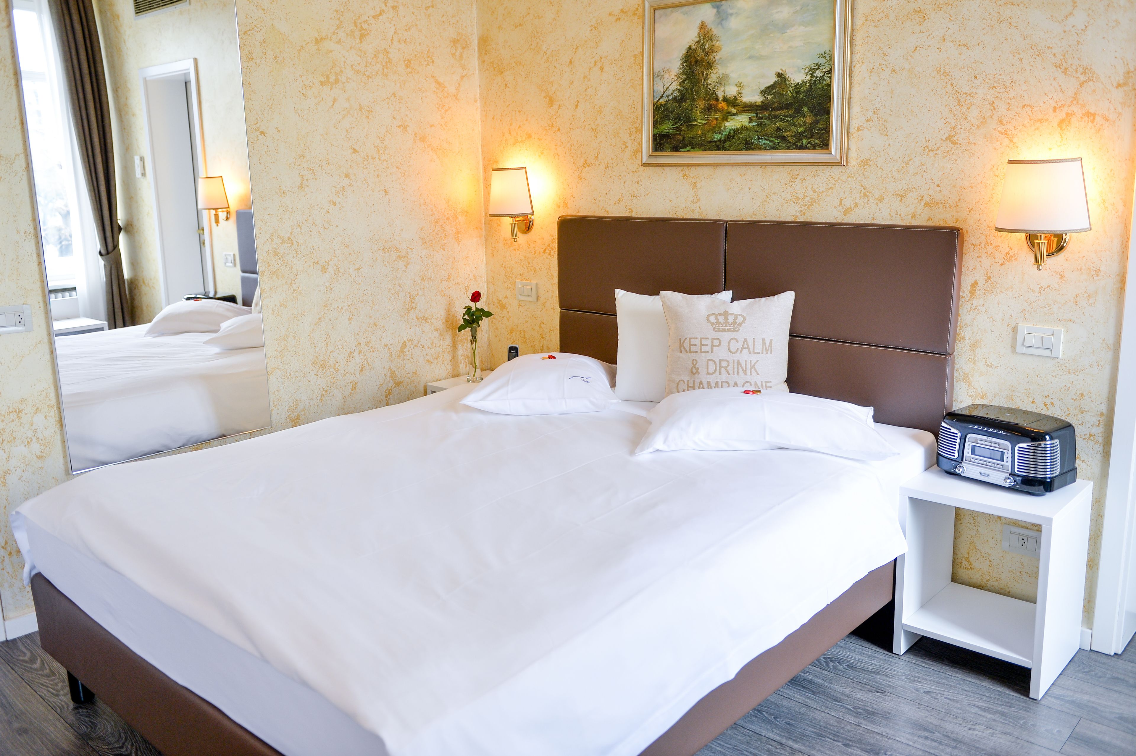 Una habitación de hotel con una cama grande, dos lámparas de noche, una mesita de noche con una radio y un cuadro en la pared.