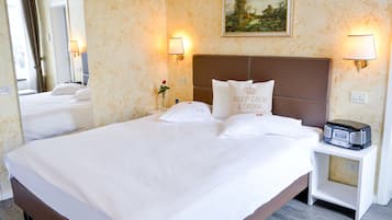 Una habitación de hotel con una cama grande, dos lámparas de noche, una mesita de noche con una radio y un cuadro en la pared.