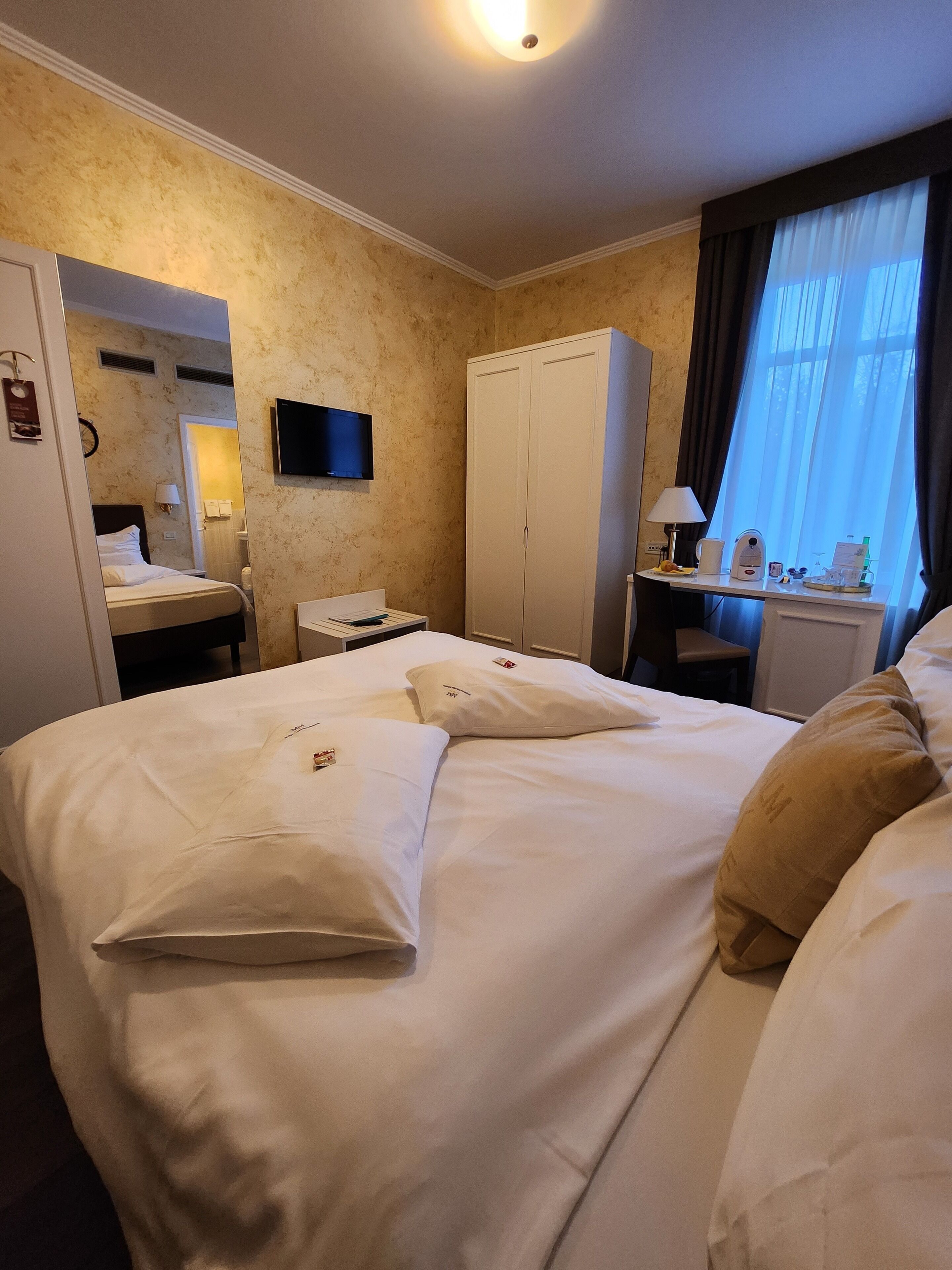 Een hotelkamer met een groot bed, een bureau met lamp, een kledingkast en een televisie aan de muur.