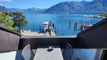 A balcony with a table and chairs overlooking a lake with boats and mountains in the background.