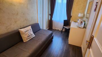 Un salon chaleureux avec un canapé marron foncé, une petite table avec une lampe et une fenêtre avec des rideaux.