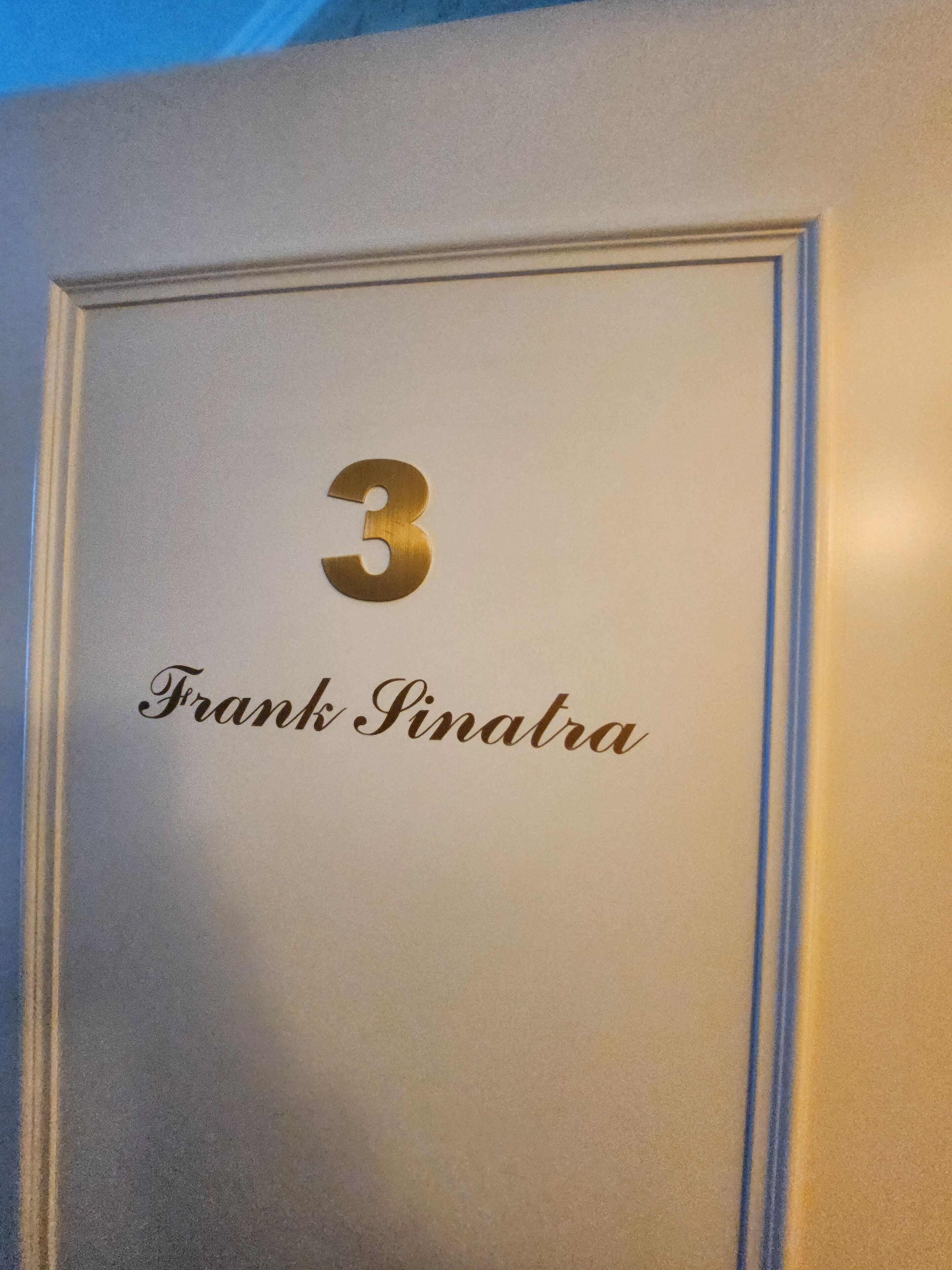 A room number plaque with the number 3 and the name "Frank Pinatra" on a wall.