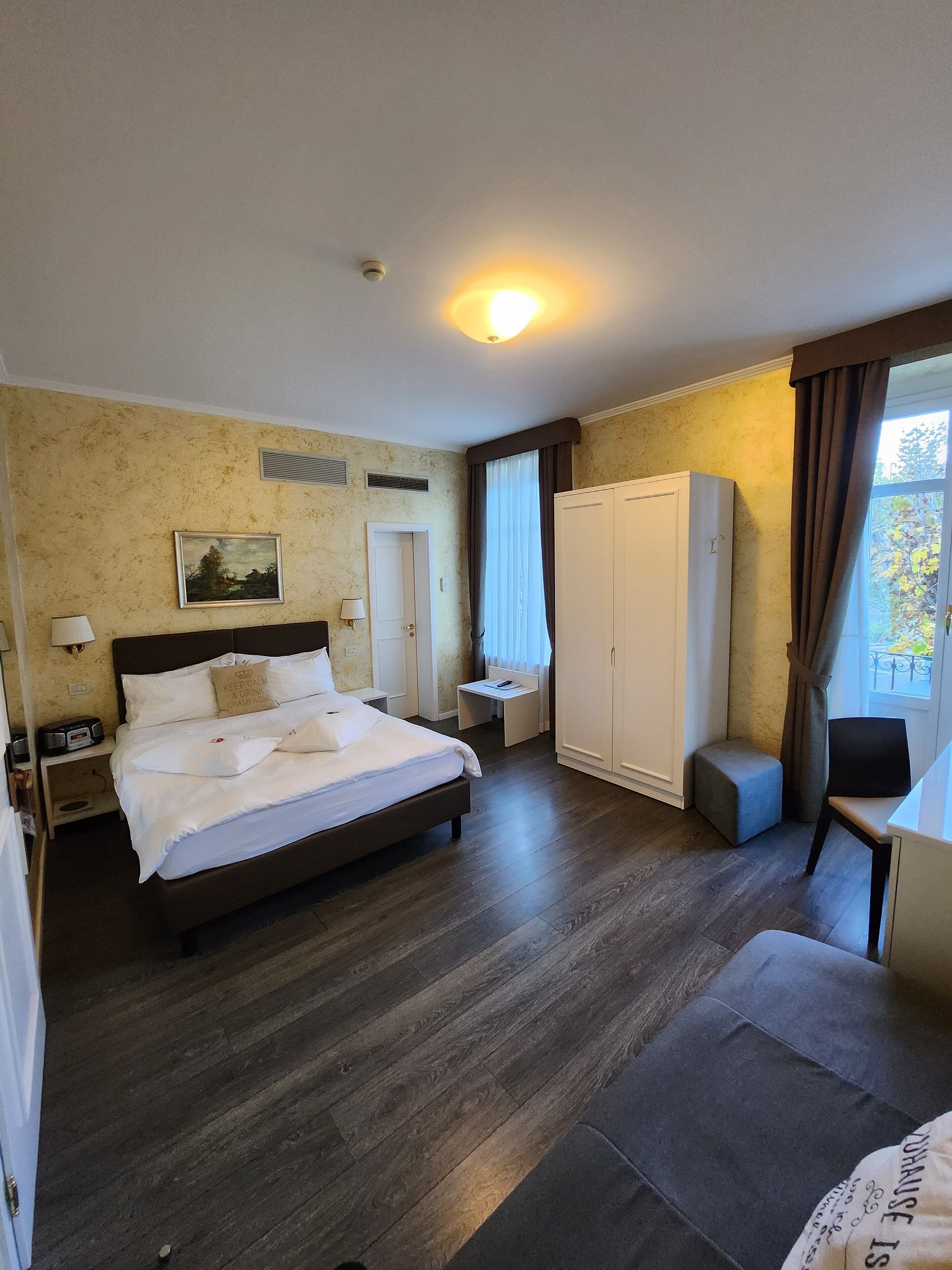 A hotel room with a large bed, a wardrobe, a desk, and a chair.