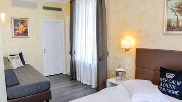 Une chambre d’hôtel comprenant un lit, un canapé-lit, une table de chevet avec une lampe, un tableau au mur et une porte.