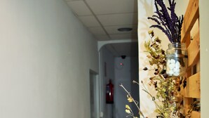 A hallway with a wooden floor, a white wall, and a wooden shelf with a vase of dried flowers. - Pension Castil (Granada)