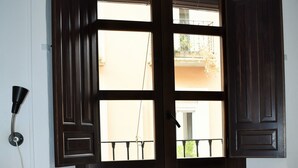 A bedroom with a large bed, a window with dark wooden shutters, and a wall-mounted lamp. - Pension Castil (Granada)