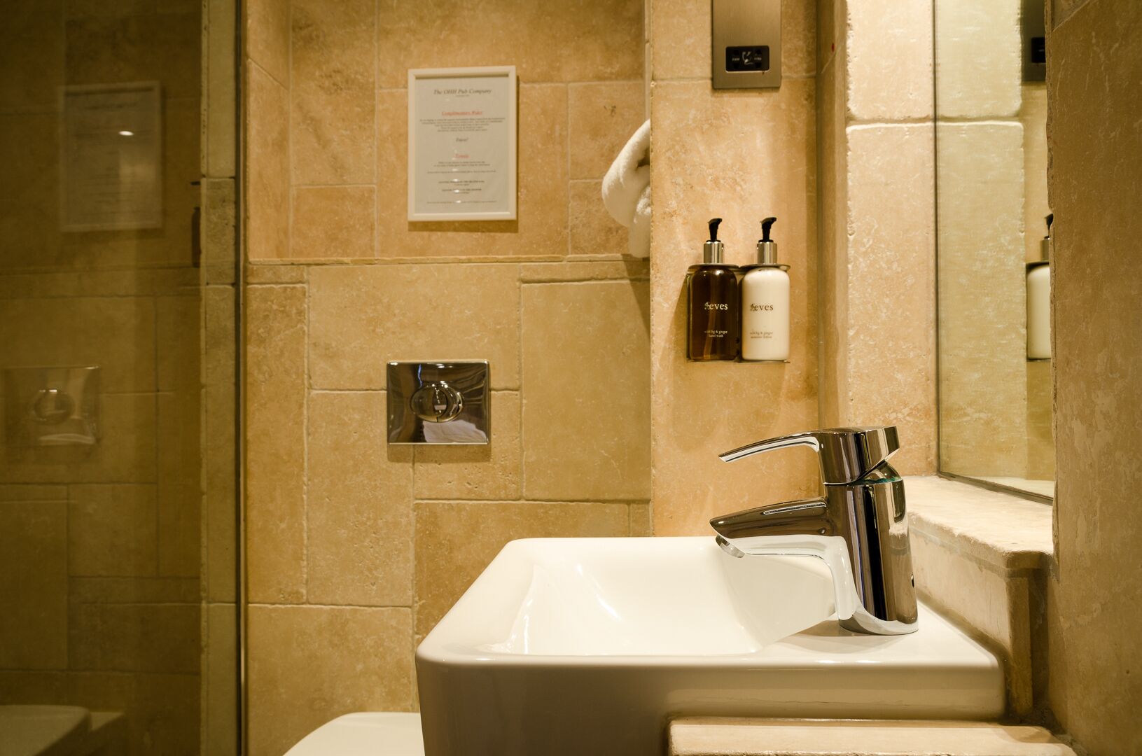 Un baño con cabina de ducha de vidrio, un lavamanos blanco con grifo cromado y artículos de aseo en una repisa.