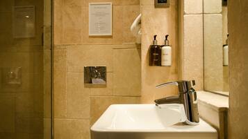 Un baño con cabina de ducha de vidrio, un lavamanos blanco con grifo cromado y artículos de aseo en una repisa.