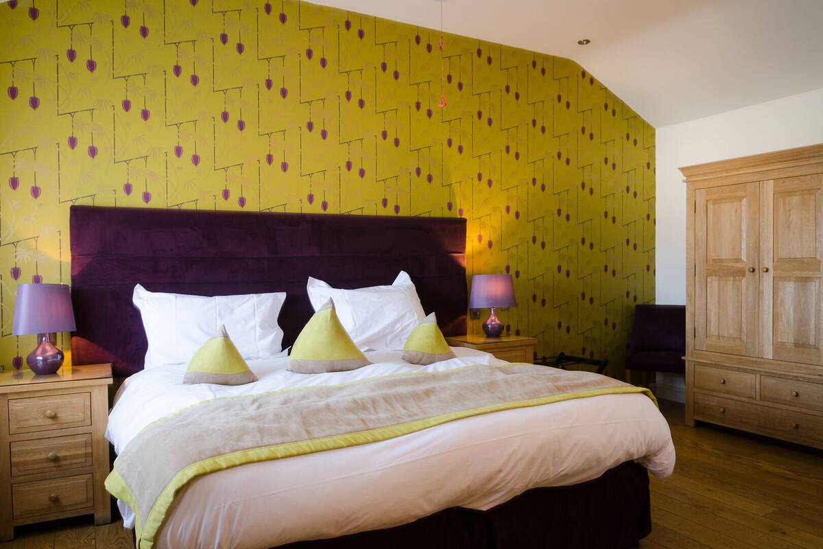 A hotel room with a large bed, two bedside tables with lamps, a wardrobe, and a patterned wall.