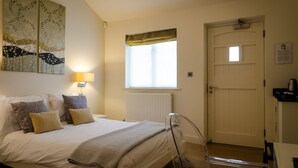 Une chambre à coucher avec un lit, des oreillers, une lampe de chevet, une fenêtre, un radiateur, une porte et une chaise.