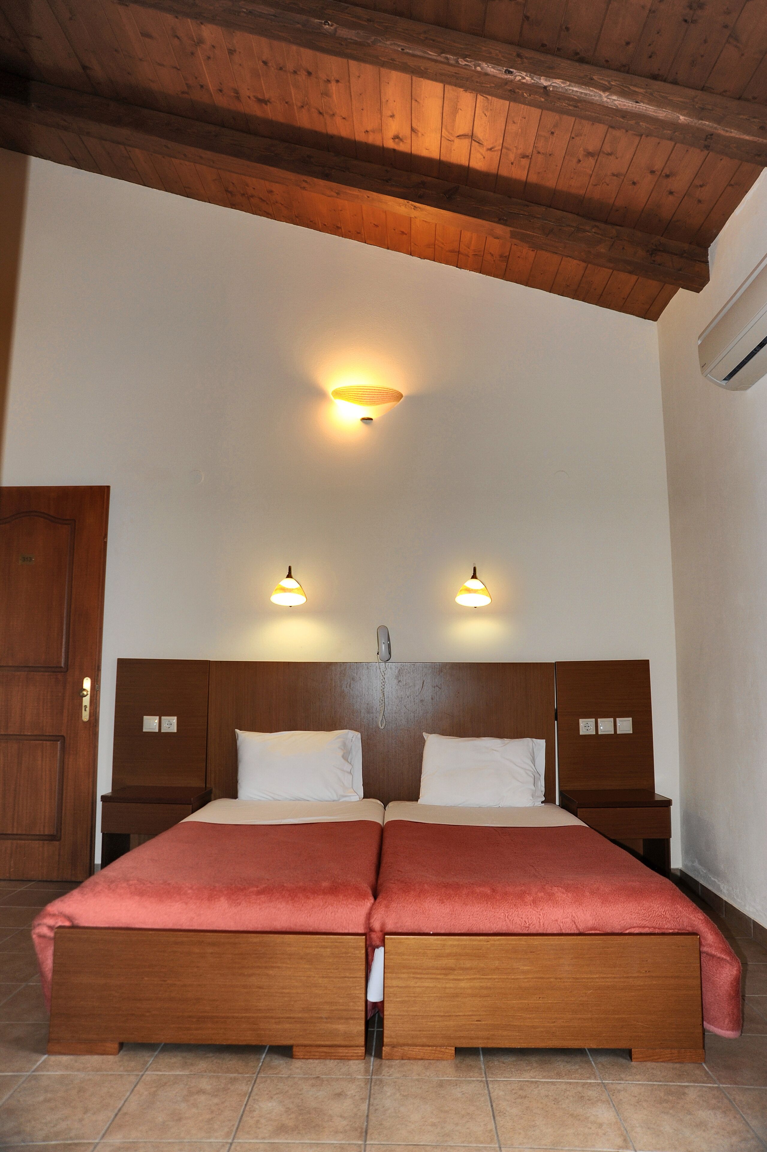Una cama doble con cabecera de madera, dos mesitas de noche y dos lámparas de pared.