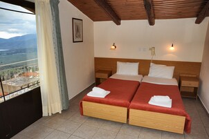Cama doble con dos almohadas, cabecera de madera, mesitas de noche, teléfono y ventana con vistas a montañas y un lago.