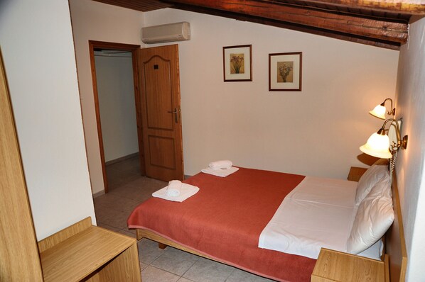 A hotel room with a bed, a wooden nightstand, a wall-mounted lamp, and two framed pictures.