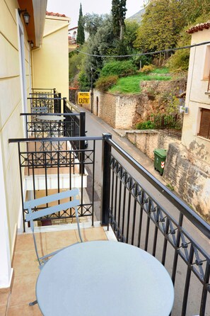 A balcony with a round table and chairs, a sign for Hotel Castri, and a stone wall with greenery.
