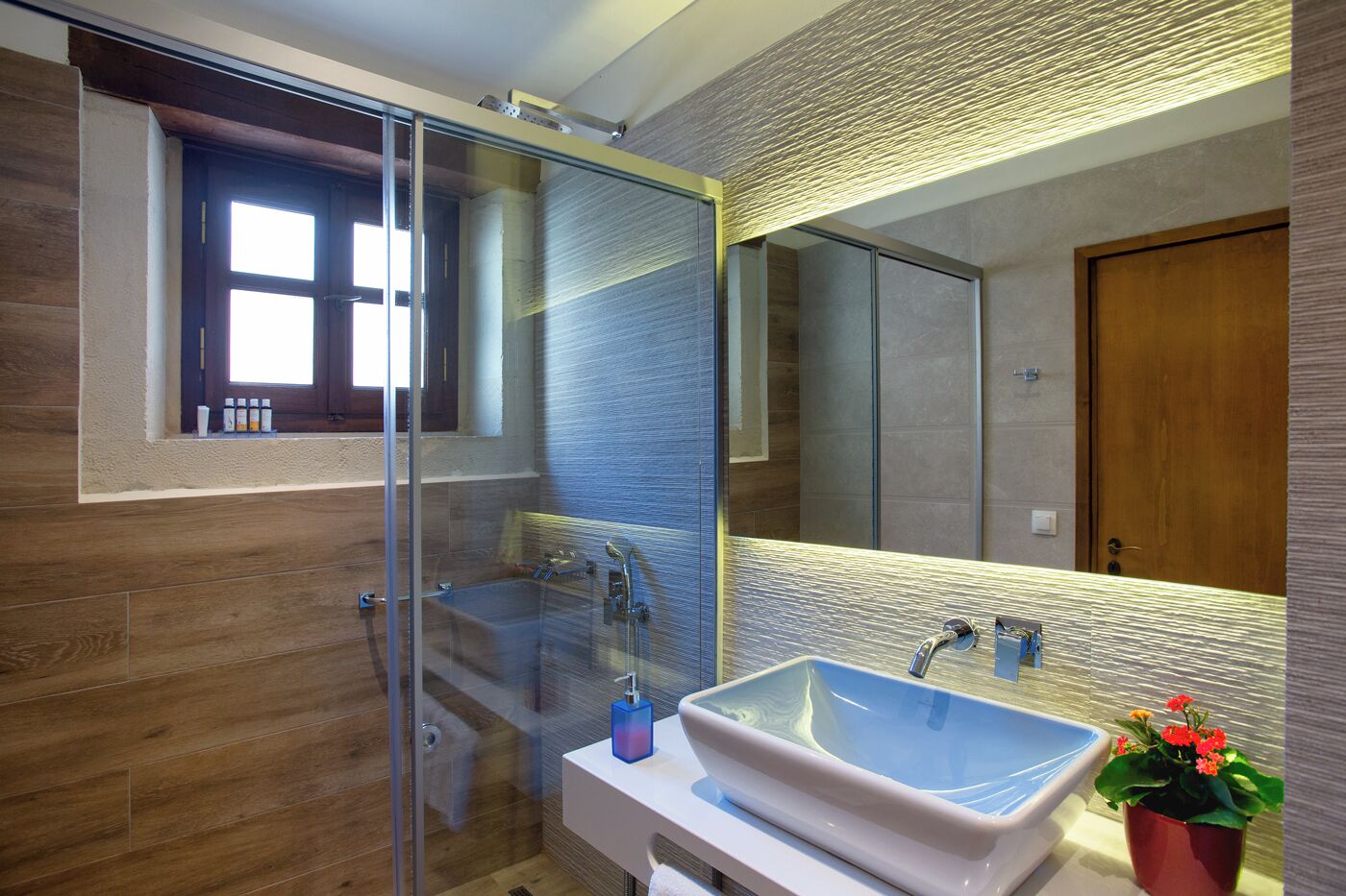 Un baño moderno con ducha de vidrio, un espejo grande y un lavabo con recipiente azul.
