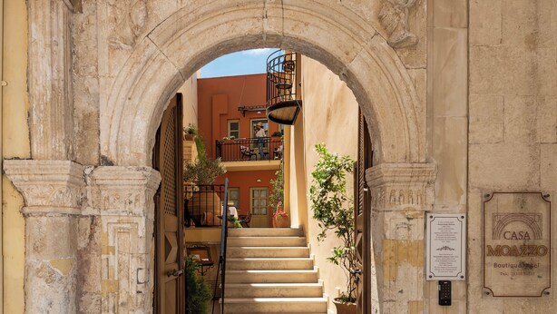 An arched doorway leading to a staircase with a view of a building in the background. - Hotel Casa Moazzo (Rethymno)