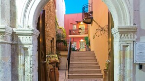 An arched entrance with a staircase leading to a building with balconies. - Hotel Casa Moazzo (Rethymno)