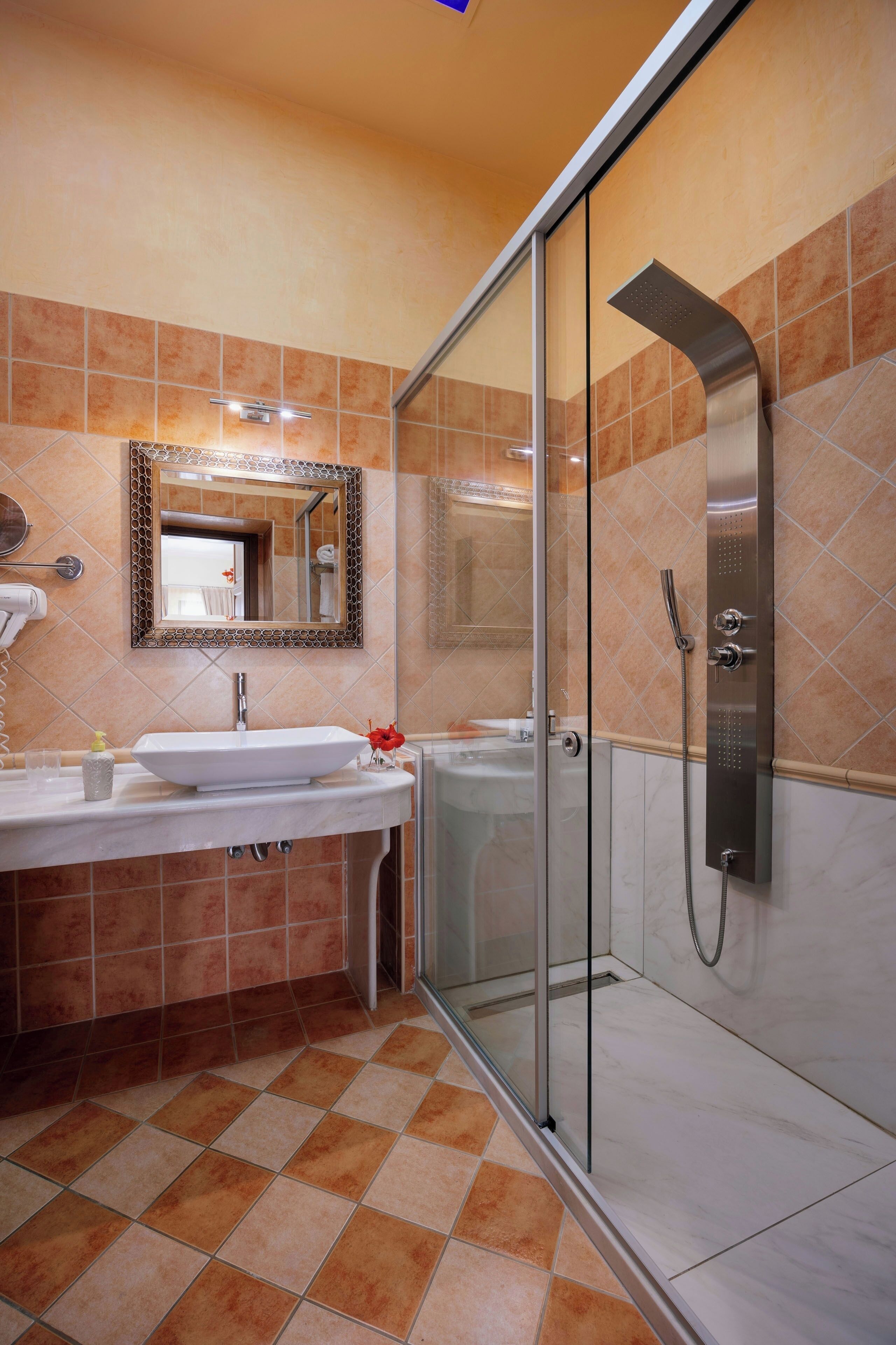 A bathroom with a glass-enclosed shower, a sink with a mirror above it, and tiled walls.