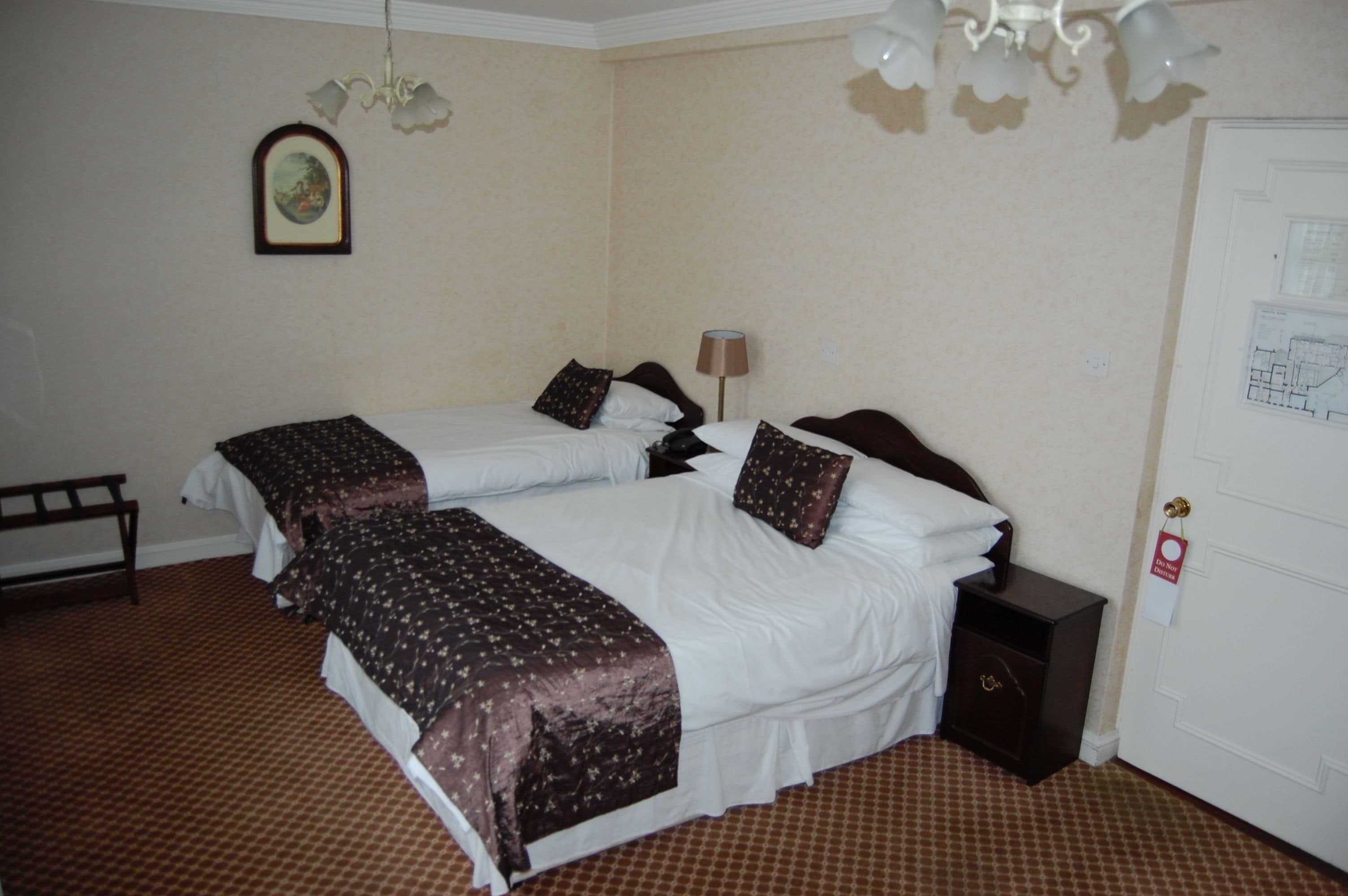 A hotel room with two beds, a nightstand, a lamp, a door with a lock, and a framed picture on the wall.
