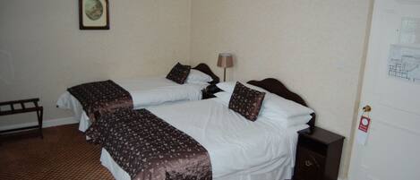 A hotel room with two beds, a nightstand, a lamp, a door with a lock, and a framed picture on the wall.