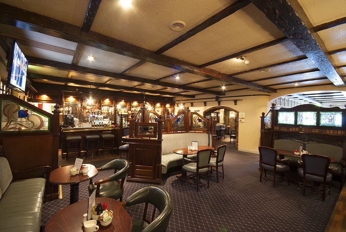 A cozy bar area with wooden beams, a bar counter, and seating arrangements including a sofa and tables.