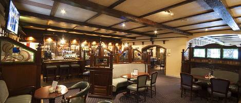 A cozy bar area with wooden beams, a bar counter, and seating arrangements including a sofa and tables.