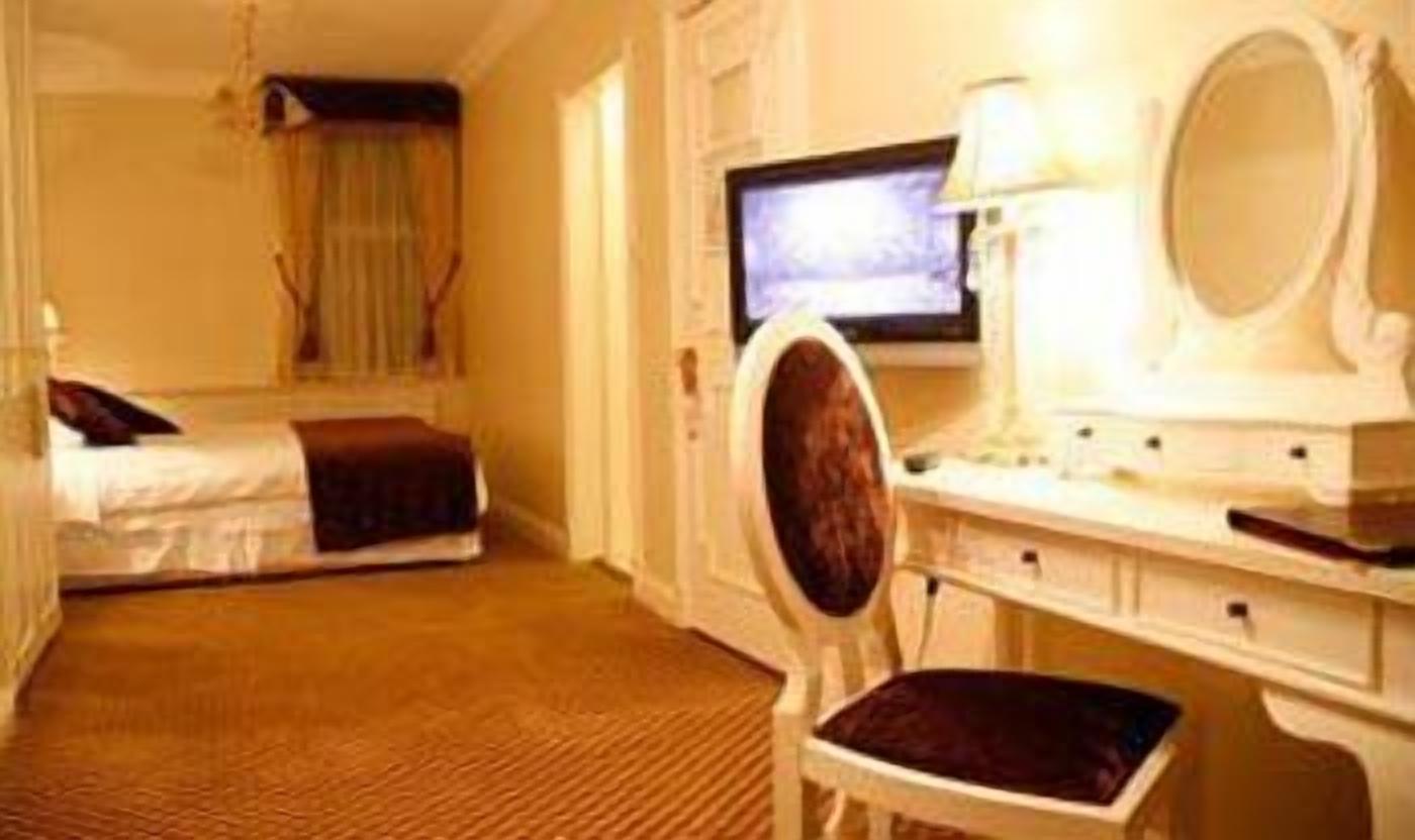 Quarto de hotel com cama, escrivaninha, computador, cadeira e televisão.